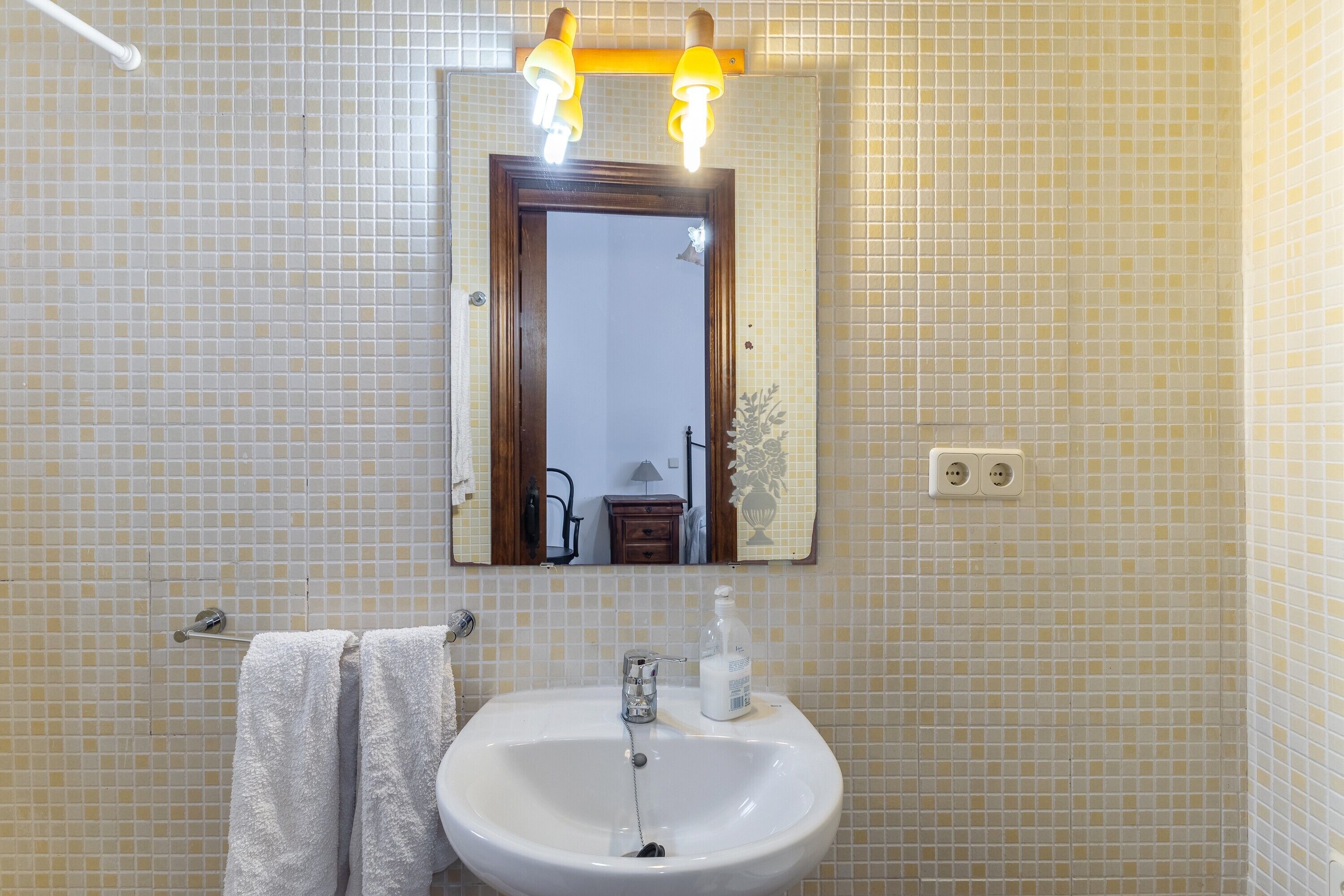 Un baño con un lavamanos blanco, un espejo y un perchero para toallas.