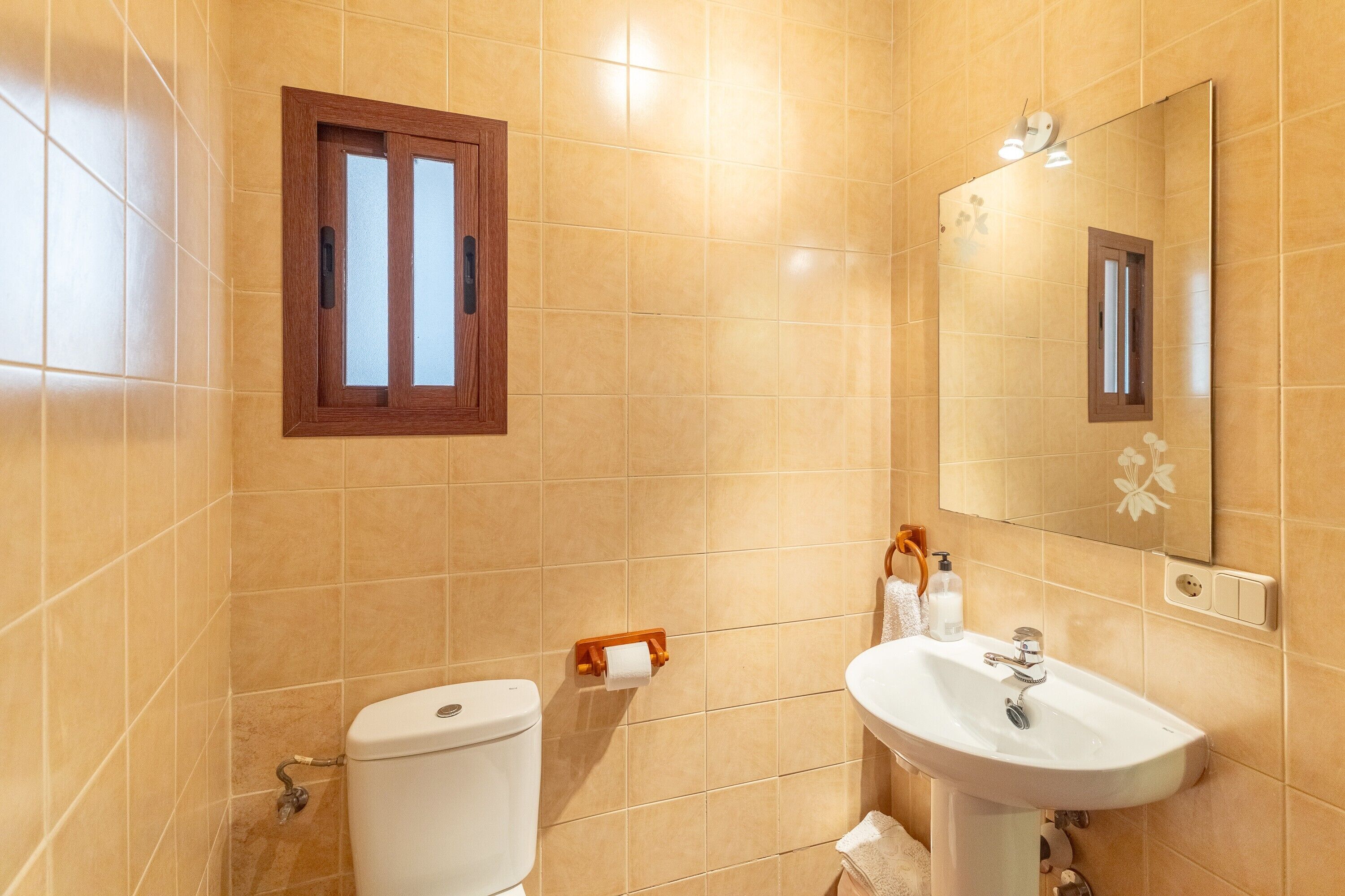 A bathroom with a toilet, sink, mirror, and a window.