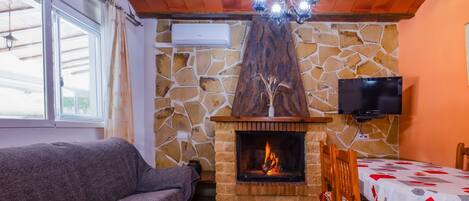 A cozy living area with a stone fireplace, a sofa, a dining table with a tablecloth, and a television mounted on the wall.