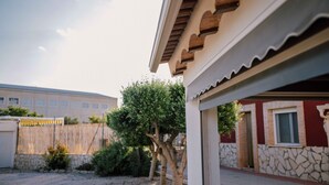 Een gebouw met een gevel van natuursteen, een houten pergola en een boom op de voorgrond.