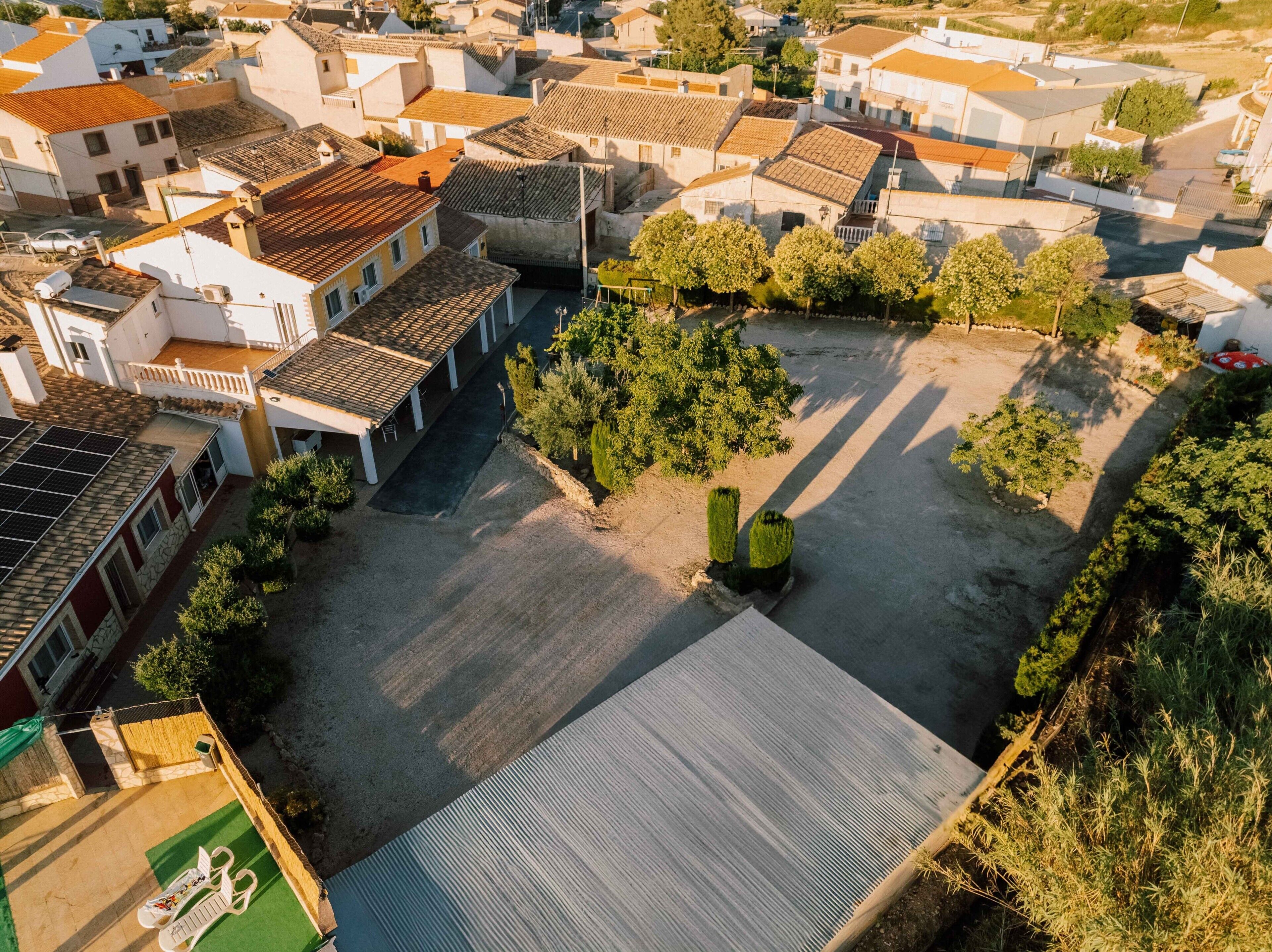 Vista aérea de una zona residencial con edificios de tejas de terracota, un patio empedrado y zonas verdes.
