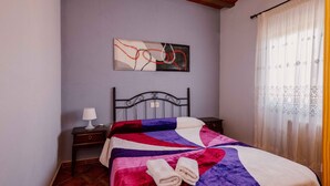 A bed with a quilt, a bedside table with a lamp, a wall art piece, and a window with curtains. - Country House 'Casa Dolores' with Mountain View, Wi-Fi and Air Conditioning (Caravaca De La Cruz)