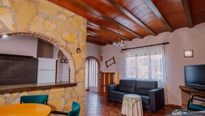 A cozy living area with a stone wall, wooden ceiling, a sofa, a TV, and a dining table. - Country House 'Casa Dolores' with Mountain View, Wi-Fi and Air Conditioning (Caravaca De La Cruz)