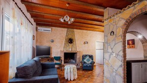 A living room with a fireplace, stone walls, a television, and a sofa. - Country House 'Casa Dolores' with Mountain View, Wi-Fi and Air Conditioning (Caravaca De La Cruz)