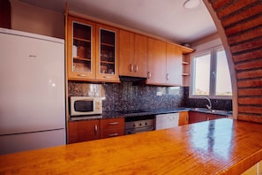 Una cocina con armarios de madera, encimera de granito, refrigerador blanco, microondas y lavavajillas.