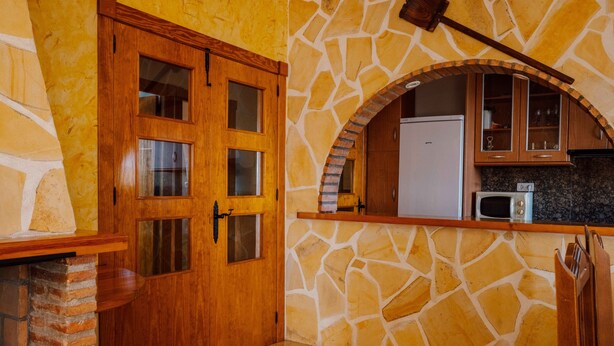 A kitchen with a stone wall, wooden cabinets, and a built-in microwave.