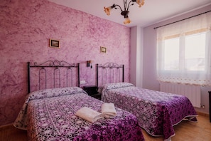 Un dormitorio con dos camas, paredes rosadas y una ventana con cortinas traslúcidas.