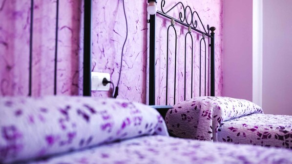 A bed with a patterned cover, a metal headboard, and a power outlet on the wall.