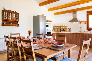 A dining area with a wooden table set for six, surrounded by chairs, with a kitchen in the background. - Rural House 'Casa Rural El Trillo' with Private Pool, Private Terrace and Wi-Fi (Aldea del Obispo (Salamanca))