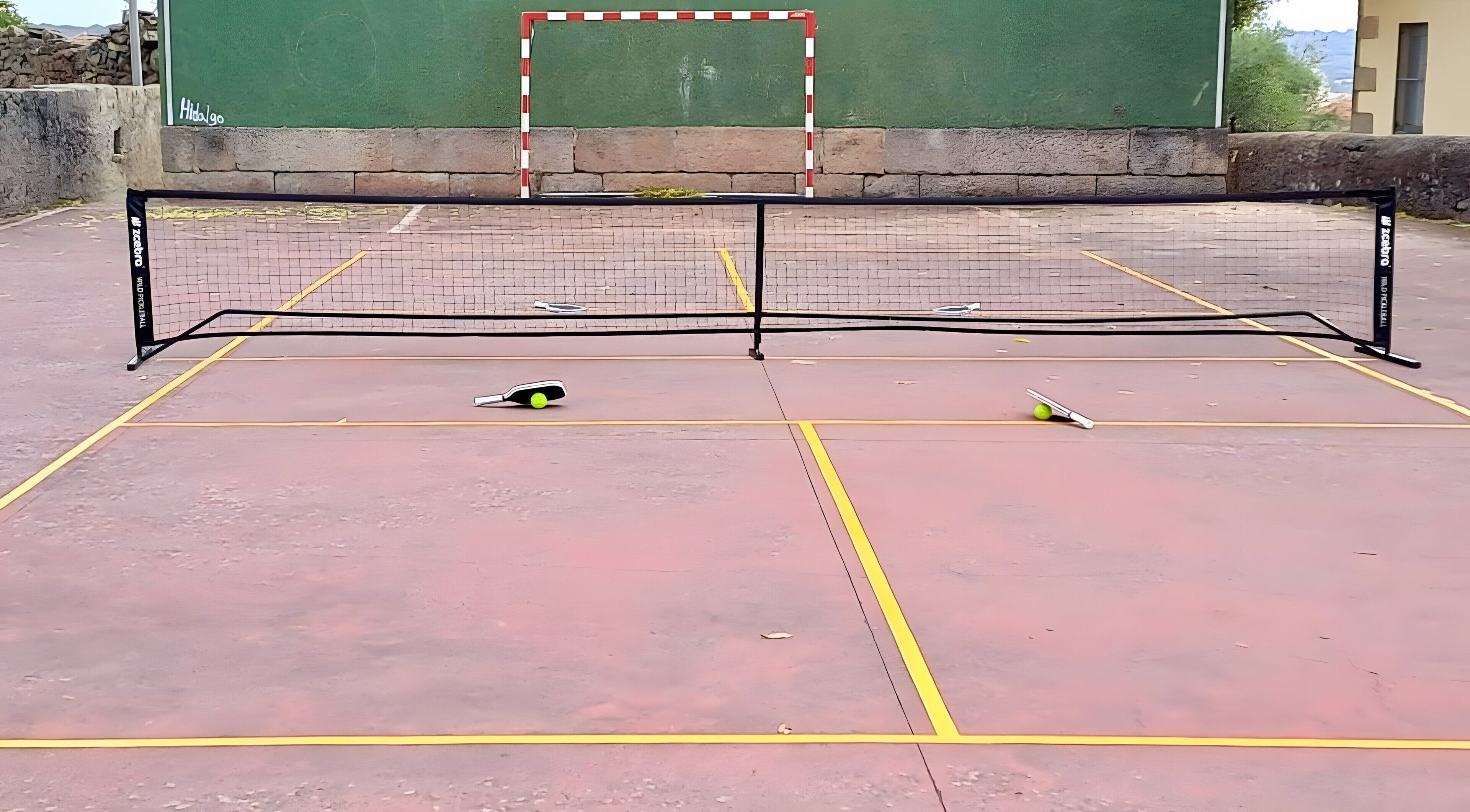 Een tennisbaan buiten met een net, een bal en een racket.