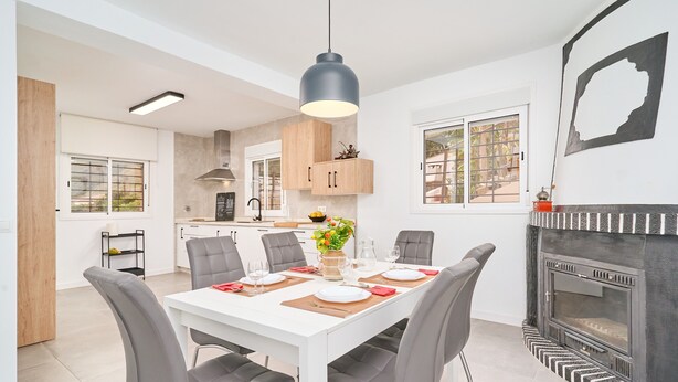 A modern kitchen with a dining area, white walls, and a fireplace.