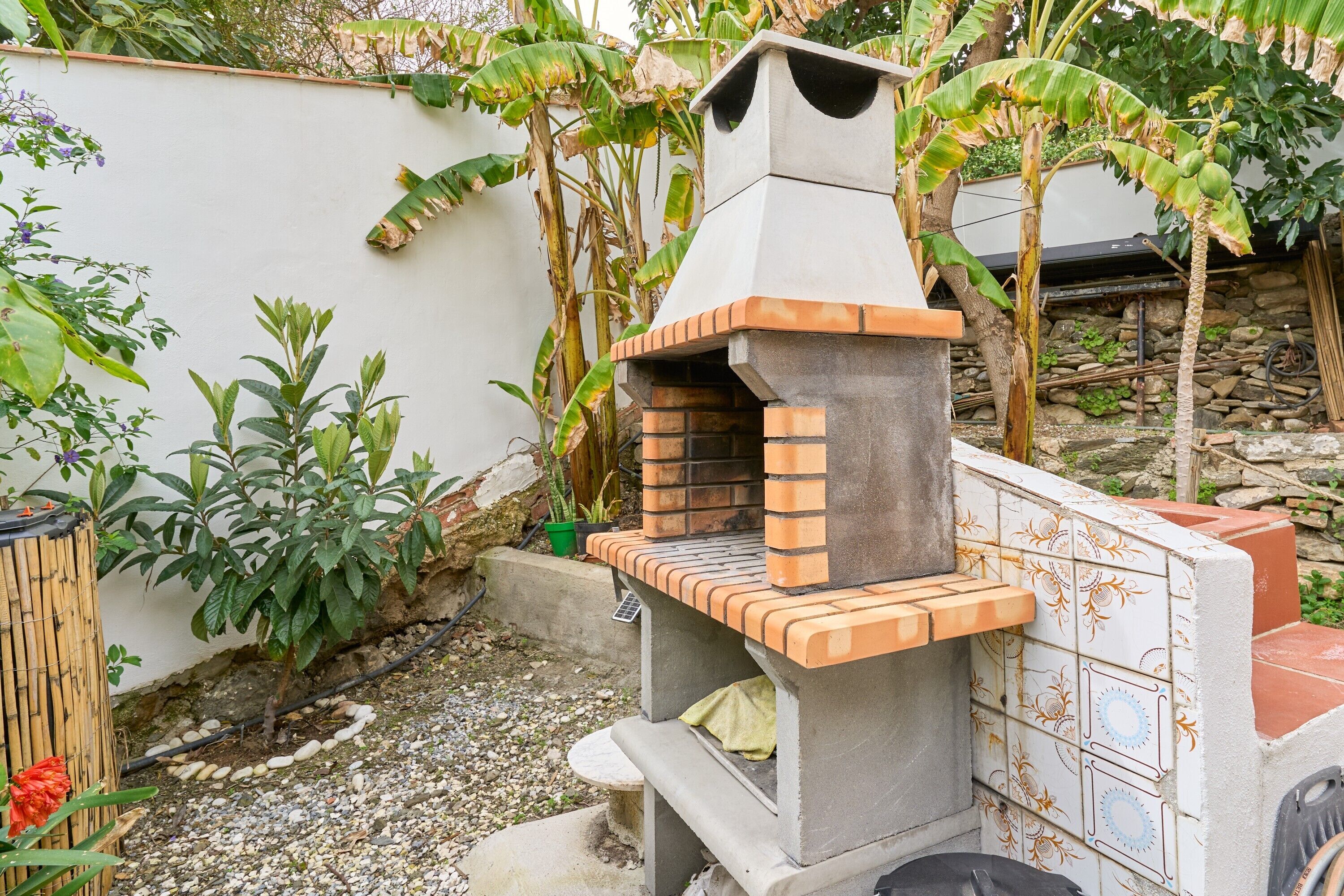A brick-built outdoor oven with a chimney, surrounded by plants and a stone wall.