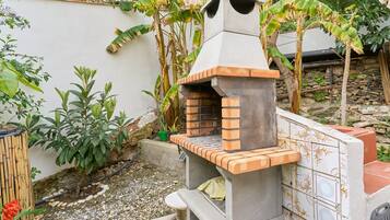 A brick-built outdoor oven with a chimney, surrounded by plants and a stone wall.