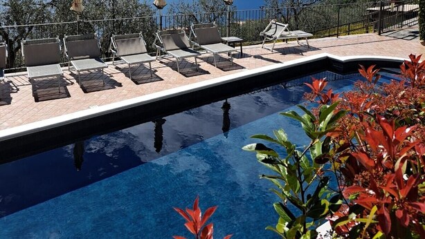 A poolside area with lounge chairs and umbrellas, overlooking a body of water and distant mountains. - Holiday Apartment "Il Cinque" with Lake View, Shared Pool & Wi-Fi (Tignale)