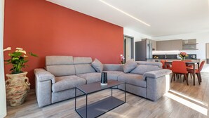 A modern living room with a grey sectional sofa, a glass coffee table, and a red accent wall. - Holiday Apartment "Il Cinque" with Lake View, Shared Pool & Wi-Fi (Tignale)