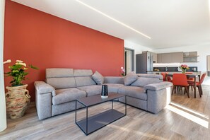 A modern living room with a grey sectional sofa, a glass coffee table, and a red accent wall.