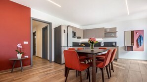 A modern kitchen with a dining area, wooden flooring, and a red accent wall. - Holiday Apartment "Il Cinque" with Lake View, Shared Pool & Wi-Fi (Tignale)