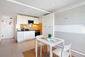 Een moderne keuken met witte kasten, een magnetron en een eethoek met een witte tafel en stoelen.