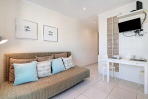 A modern living room with a sofa, a desk, and a flat-screen TV. - Studio Apartment 'Estúdio Completo' with Sea View, Wi-Fi and Air Conditioning (Albufeira)