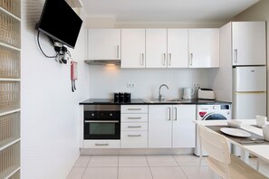 A modern kitchen with white cabinets, a black countertop, a built-in oven, a microwave, a sink, and a flat-screen TV mounted on the wall. - Studio Apartment 'Estúdio Completo' with Sea View, Wi-Fi and Air Conditioning (Albufeira)