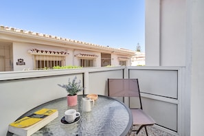 A glass table with a book, coffee cup, and pitcher on a balcony with a chair and a potted plant. - Apartment 'Calm Bungalow' with Shared Pool, Wi-Fi and Air Conditioning (Torrox)
