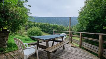 Een houten terras met een picknicktafel en stoelen, met uitzicht op een bebost gebied.