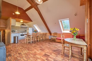 A cozy kitchen with wooden beams, a dining area with hexagonal patterned flooring, and a window with a view.