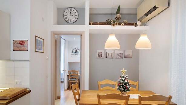 A dining area with a wooden table and chairs, a small Christmas tree, and a clock on the wall.