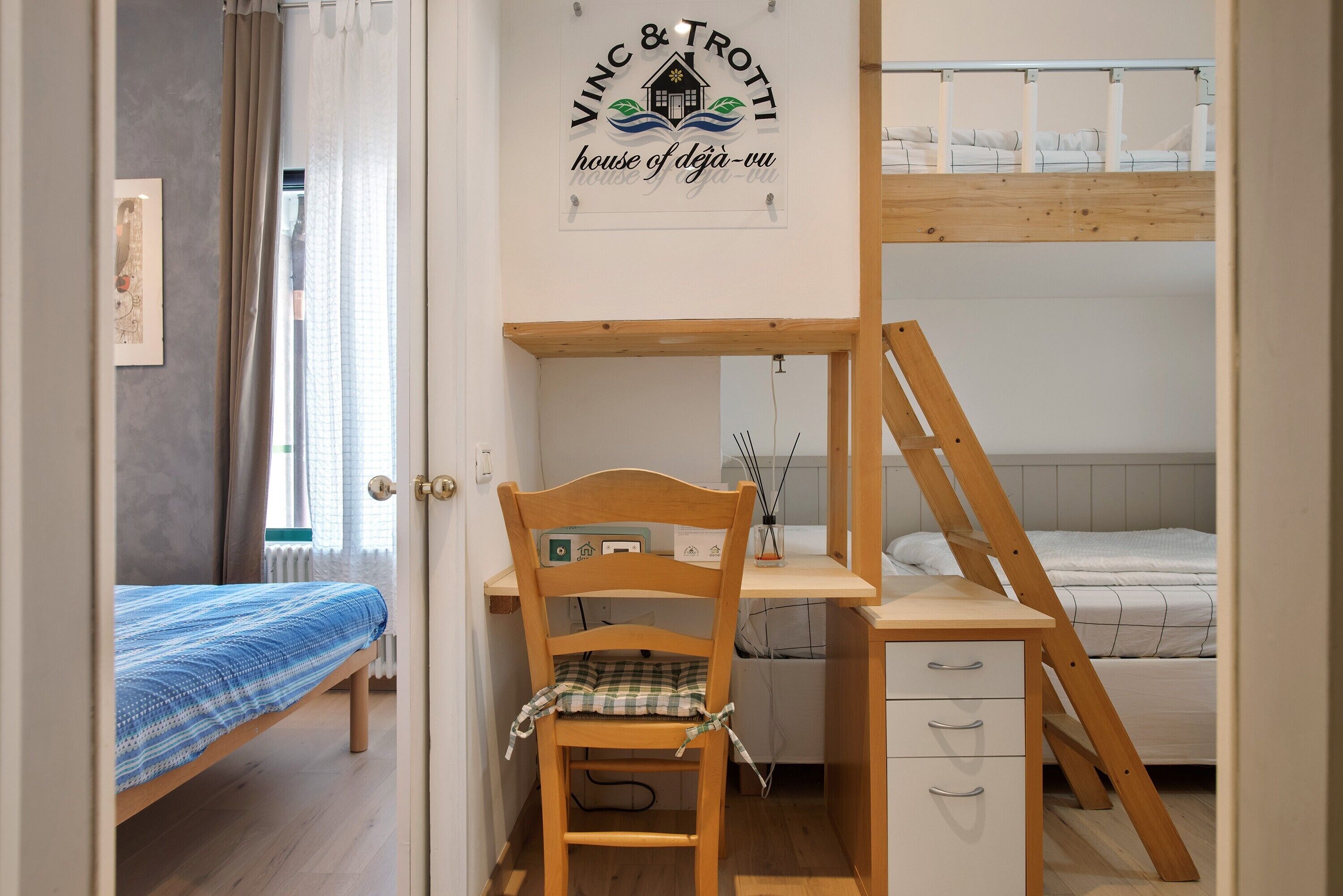 Una habitación con literas, un escritorio con silla, una cama pequeña y un letrero en la pared.