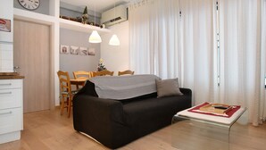 A modern living room with a black sofa, a glass coffee table, wooden chairs, a dining table, and a small Christmas tree.