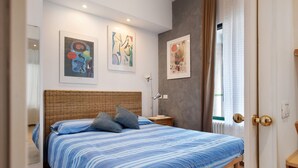 A bedroom with a bed, a nightstand, a lamp, and artwork on the wall.