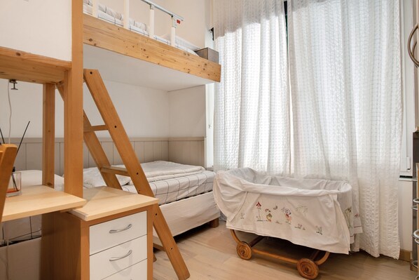 Habitación con literas, un escritorio, un cochecito de bebé y una ventana con cortinas.
