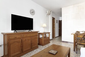 Ein Wohnzimmer mit Flachbildfernseher, Holzmöbeln, einer Lampe und einer Wanduhr.