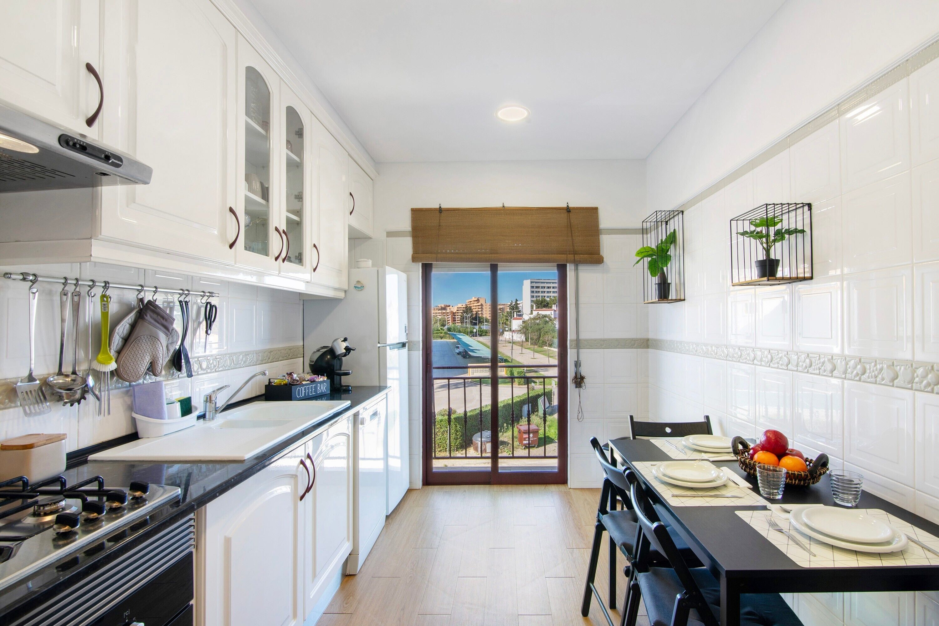 A modern kitchen with white cabinets, a dining area with a table set for two, and a view through a glass door.
