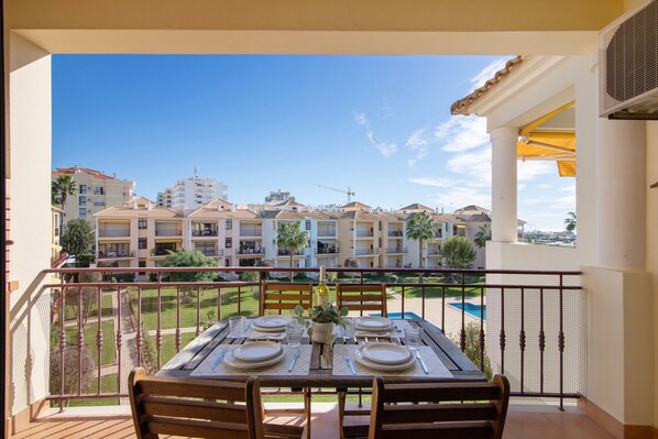 A balcony with a table set for dining, overlooking a residential area with buildings and a clear sky.