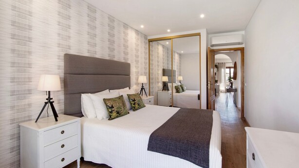 A modern hotel room with a large bed, bedside tables, a mirror, and a hallway leading to a bathroom.
