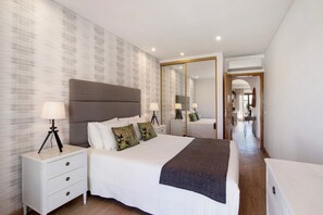 A modern hotel room with a large bed, bedside tables, a mirror, and a hallway leading to a bathroom.