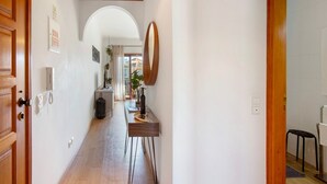 A hallway with a wooden door, a mirror, a table with a bottle, and a plant.