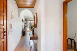 Un couloir avec une porte en bois, un miroir, une table avec une bouteille et une plante.