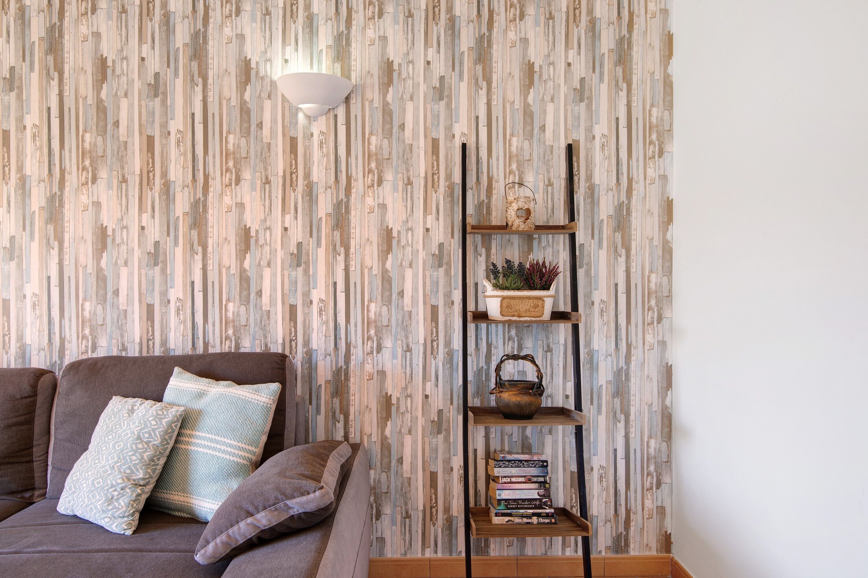 Una sala de estar con pared estampada, un sofá con cojines, un estante de pared con adornos y una lámpara.