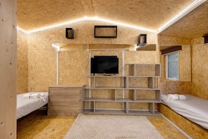 A compact room with a bed, a TV, a wooden dresser, and built-in shelving.