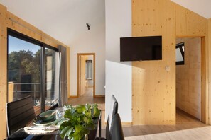 Un intérieur moderne comprenant un coin repas, de grandes fenêtres et un téléviseur à écran plat fixé au mur.