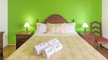 Une chambre d’hôtel avec un mur vert, une tête de lit en bois, un lit recouvert d’une courtepointe matelassée, deux tables de chevet avec des lampes et deux serviettes enroulées posées sur le lit.