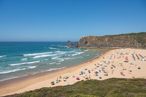 Una playa con gente, sombrillas y un acantilado.