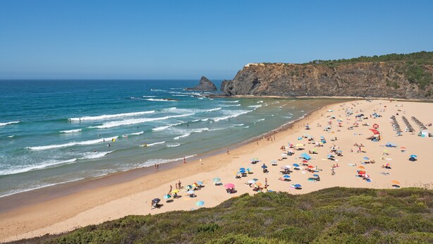 A beach with people, umbrellas, and a cliff.