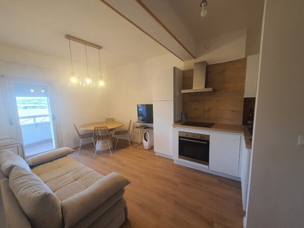 A modern kitchen with a dining area, a sofa, and a TV.