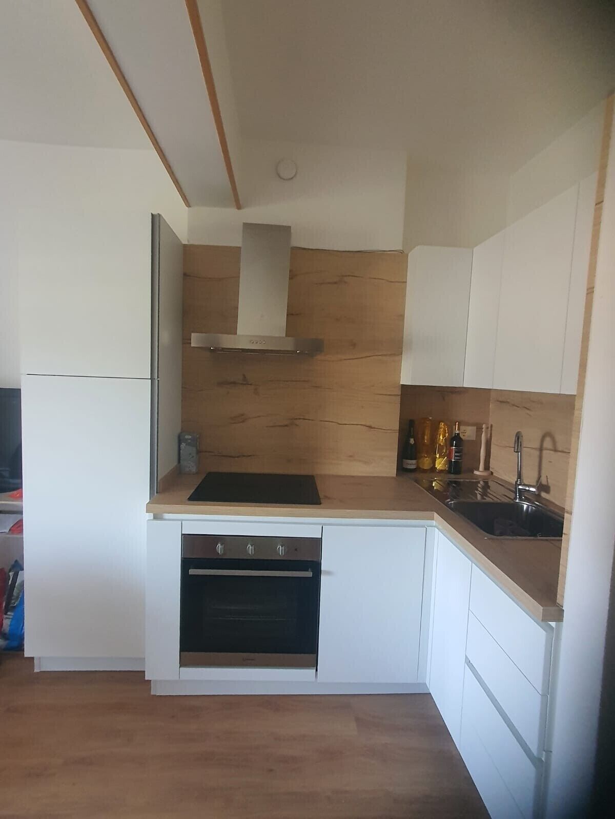 A compact kitchen with white cabinetry, a built-in oven, a stainless steel sink, and a wooden backsplash.