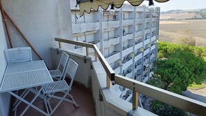 En balkong med ett bord och stolar, utsikt över ett bostadshus och en klar himmel.