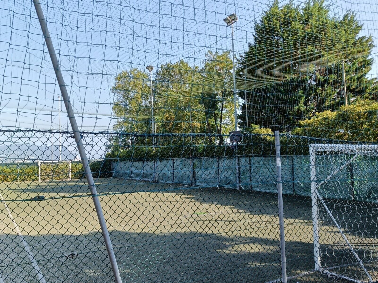 Ein eingezäunter Sportplatz mit Tor, umgeben von Bäumen und einem klaren Himmel.