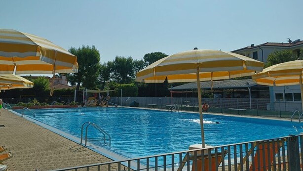 En swimmingpool med flera gula parasoller med ränder, en klarblå himmel och en byggnad i bakgrunden.